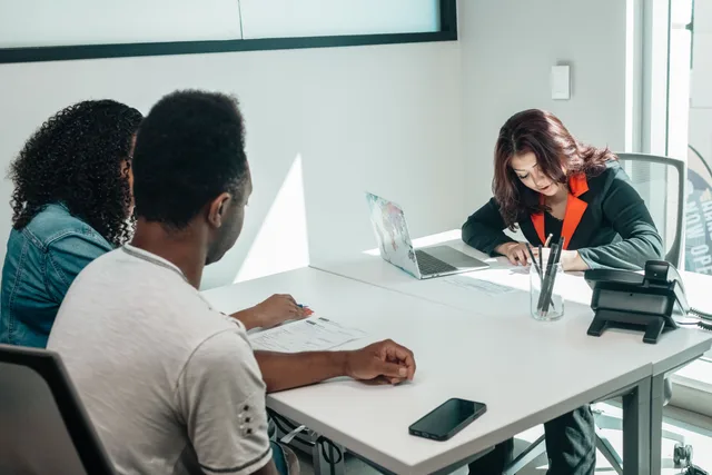 A couple discussing paperwork with an advisor in a modern office setting, showcasing collaboration. 3 things to check in talent management agency services