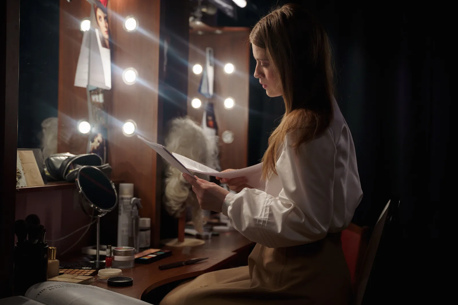 A woman in a dressing room reading a script, surrounded by makeup and lights. Talent management agency startup: roles, contracts, and state registration
