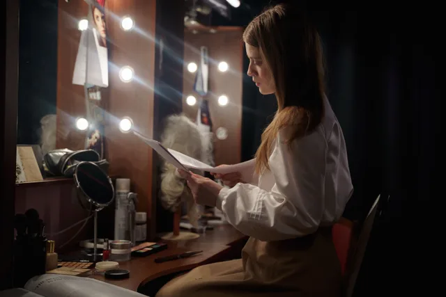 A woman in a dressing room reading a script, surrounded by makeup and lights. Talent management agency startup: roles, contracts, and state registration