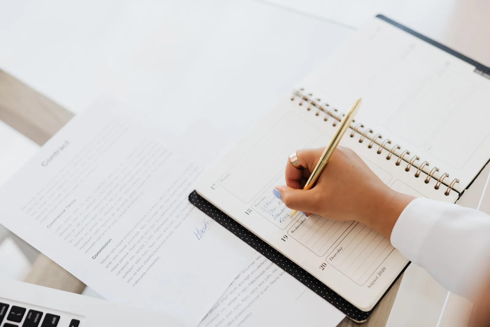 Close-up of a person writing in a planner next to a contract document on a desk. Contract terms: what a talent agency should never leave out